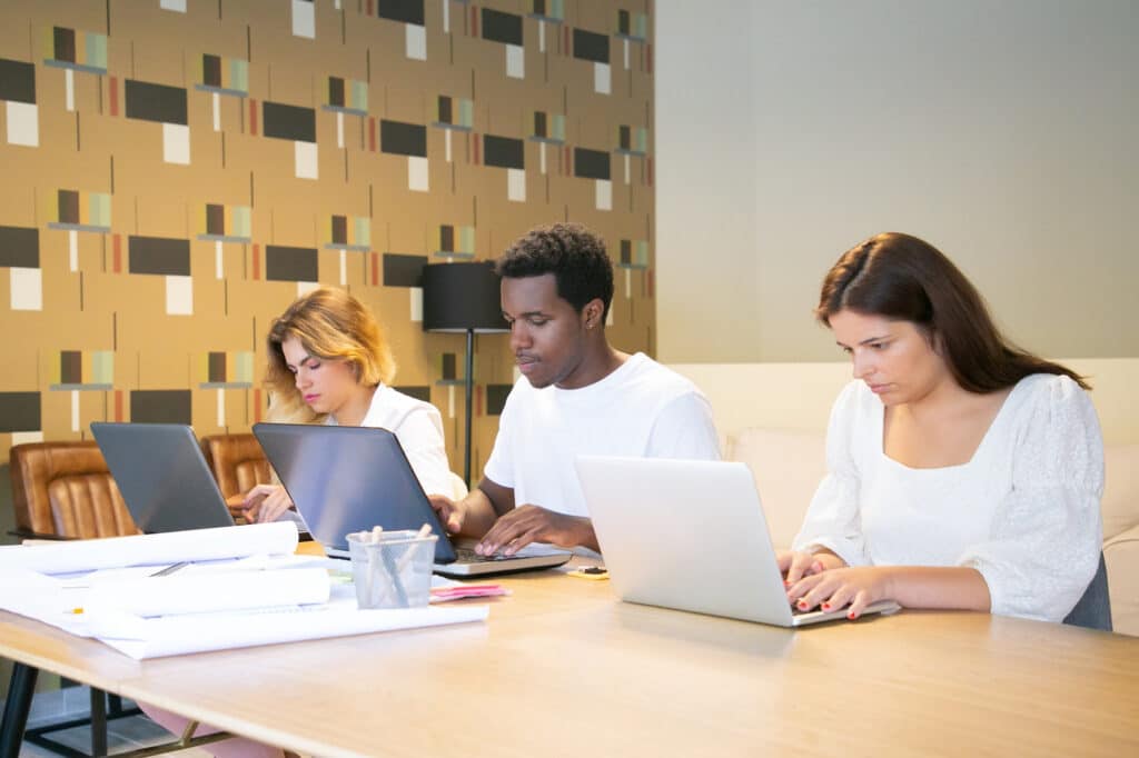 Graduate students working on laptops and application documents in a modern study space